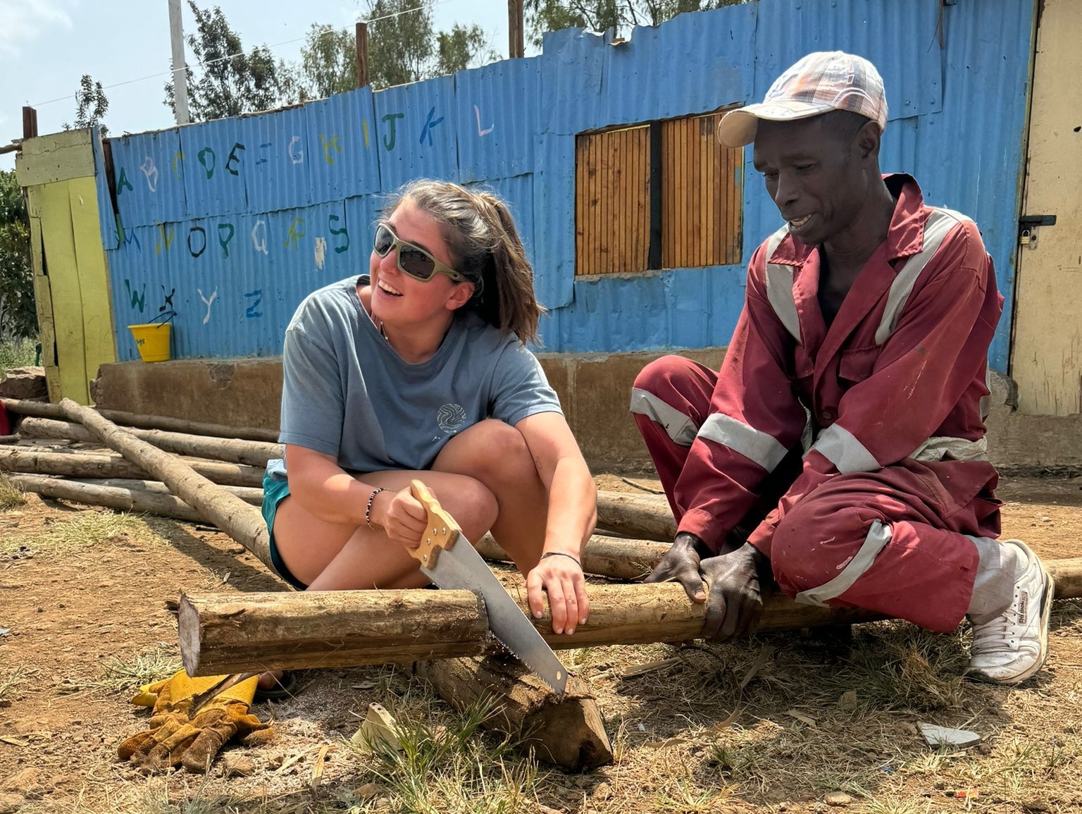 Volunteer cutting wood with help of local worker at Malaika School, Kibra, Nairobi.